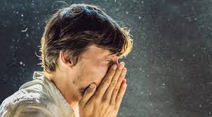 A man sneezing into his hands with visible particles in the air, illustrating a reaction to poor air quality indoors.